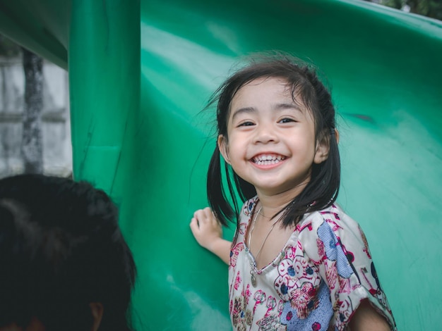 Retrato de una niña linda y sonriente deslizándose en el patio de recreo