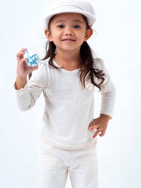 Foto retrato de una niña linda sosteniendo un huevo de pascua mientras está de pie contra un fondo blanco