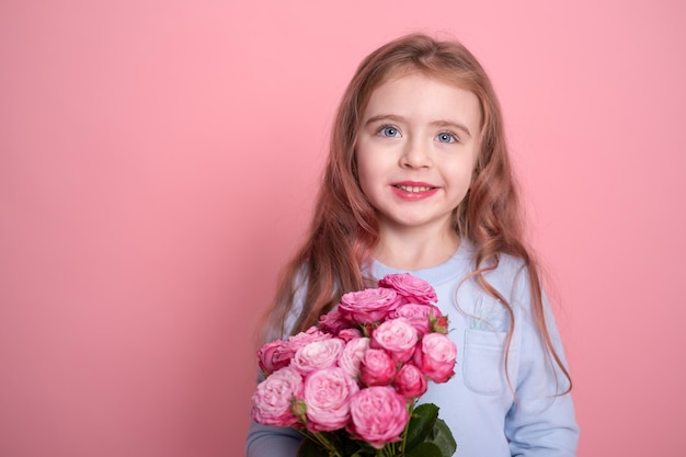 Retrato de niña linda en vestido azul con ramo de rosas rosadas sobre fondo rosa