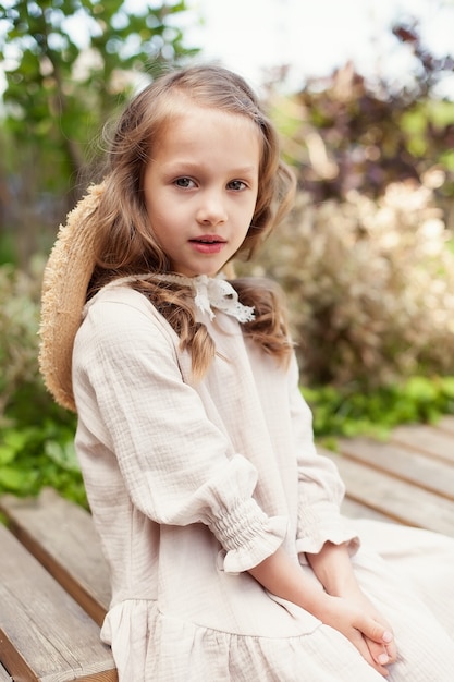 Retrato de una niña linda con un vestido beige en un día de verano en el parque. la niña mira a la cámara y sonríe.