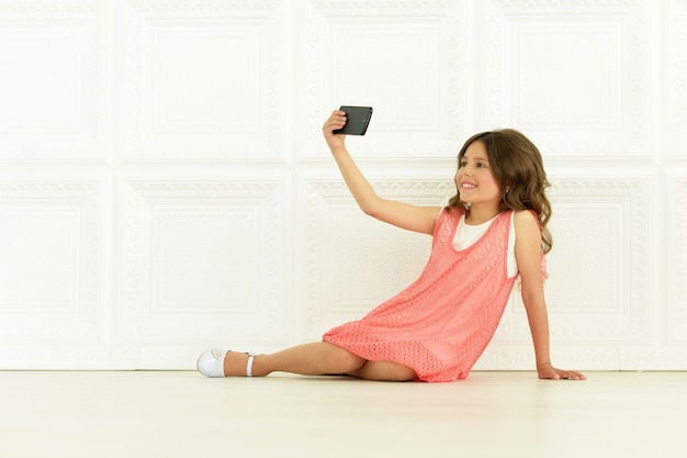 Retrato de niña linda en vestido hermoso con teléfono móvil tomando foto selfie