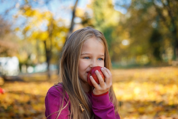 Retrato de una niña con una manzana en la mano en el parque otoño