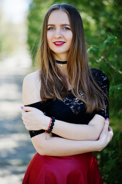 Retrato de niña con maquillaje brillante con labios rojos, collar de gargantilla negra en el cuello y falda de cuero rojo.