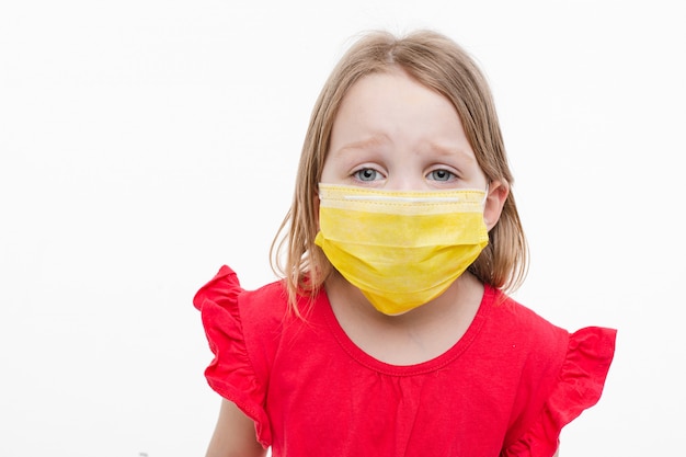 Retrato de niña con máscara médica amarilla en su rostro tiene miedo, aislado sobre fondo blanco.