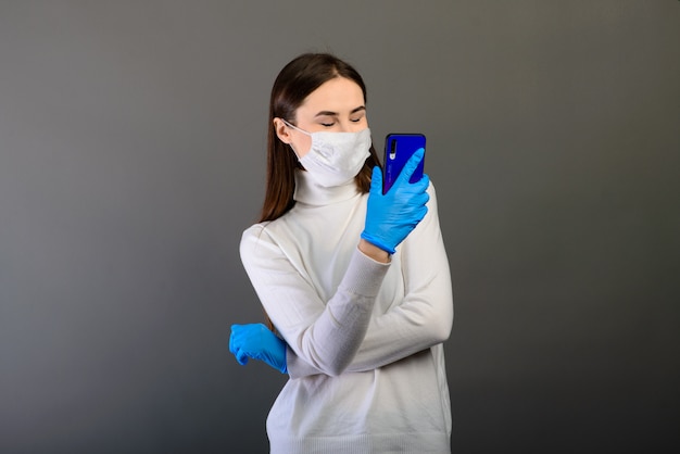 Retrato de una niña en una máscara médica con un teléfono