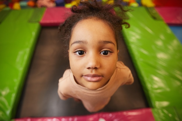 Retrato de niña mirando al frente mientras salta en un trampolín en el parque de atracciones