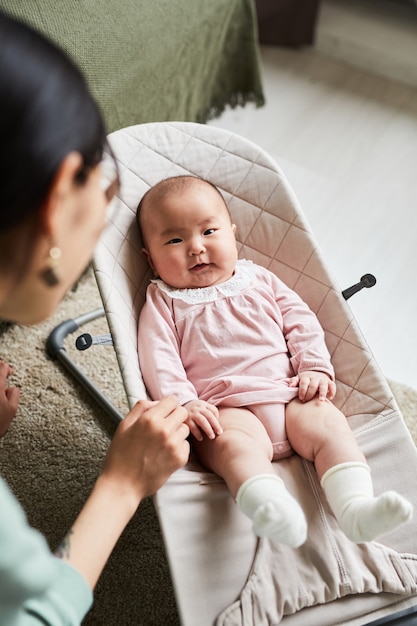 Retrato de niña mirando a la cámara mientras la madre la acuna en una silla longue en la habitación de casa