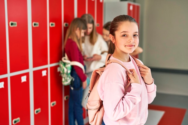 Retrato de una niña con una mochila de pie en el pasillo de la escuela