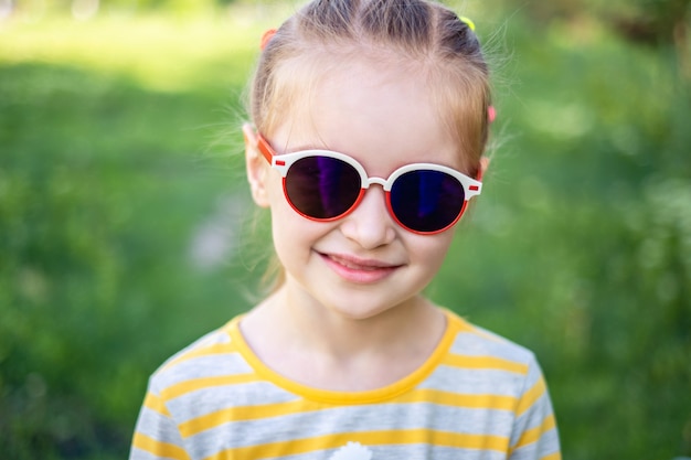 Retrato de niña de moda en gafas de sol bonitas modernas en el fondo del parque verde