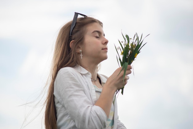 Retrato de una niña de moda con un ramo de flores silvestres en un campo verde sobre un fondo de cielo nublado