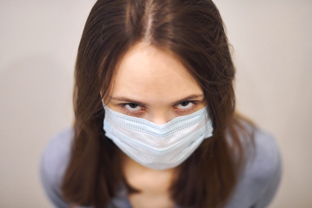 Retrato de niña molesta en máscara médica protectora, mirando con desconfianza