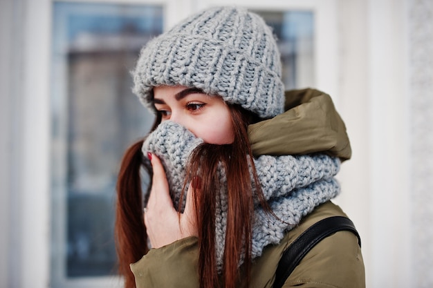 Retrato de niña morena con bufanda gris y sombrero en clima frío.