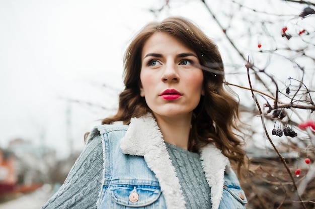 Retrato de niña morena en chaqueta de jeans en arbustos congelados.