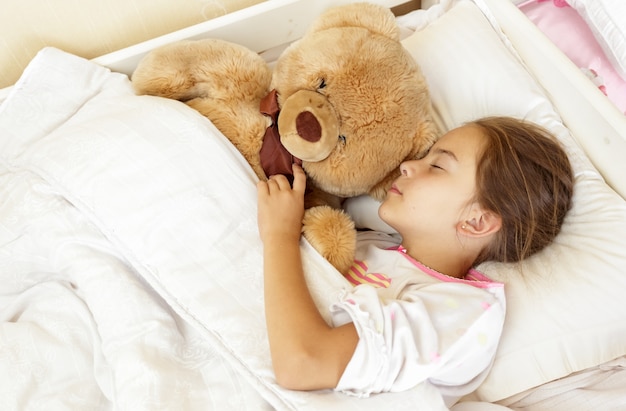 Retrato de niña morena durmiendo en la cama con osito de peluche