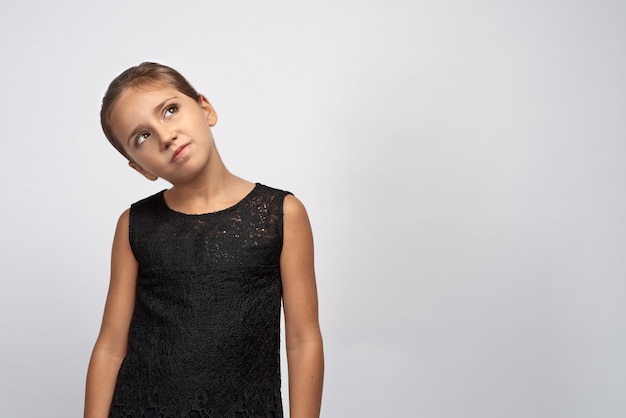 Retrato de niña morena pensativa en un vestido negro. Hermoso niño dudoso e indeciso que mira los ojos pensativos, con una expresión perpleja que piensa algo.