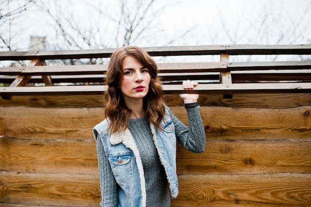 Retrato de niña morena rizada en chaqueta de jeans contra la pared de madera.