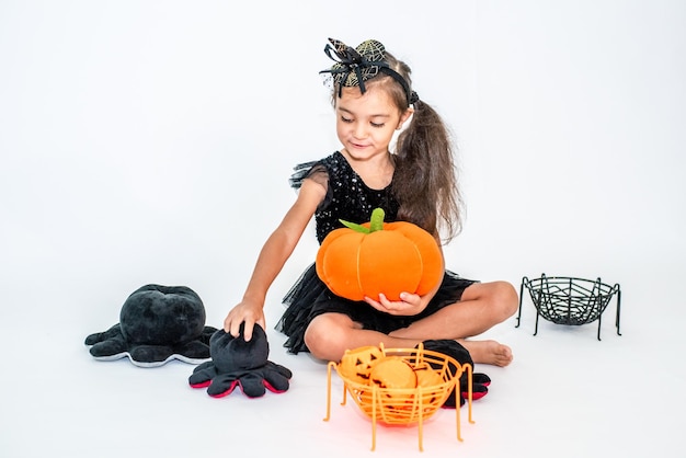 retrato de una niña morena con un sombrero negro y un vestido negro con decoraciones de Halloween.