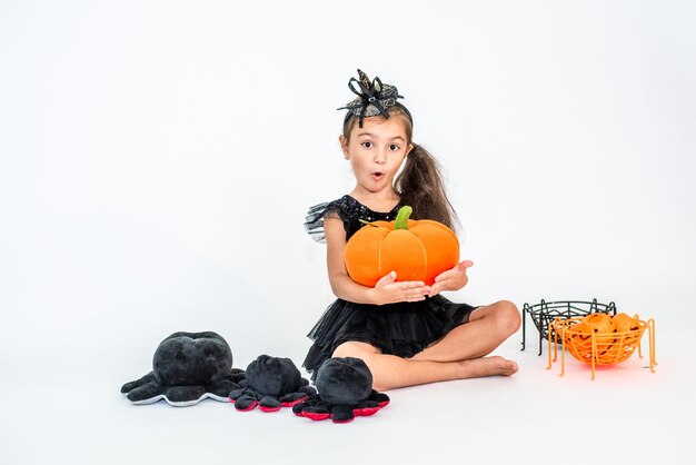 retrato de una niña morena con un sombrero negro y un vestido negro con decoraciones de Halloween.