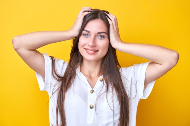 Retrato de niña morena sosteniendo su cabeza sonriendo y regocijándose aislado sobre fondo amarillo