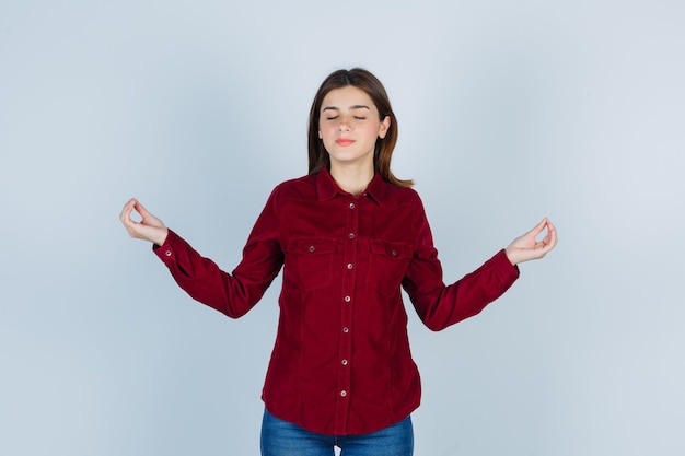 Retrato de niña mostrando gestos de yoga en blusa burdeos y buscando pacífica