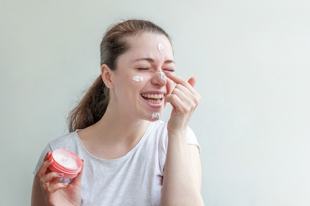 Retrato de niña mujer aplicando mascarilla nutritiva blanca o crema en la cara aislada en blanco