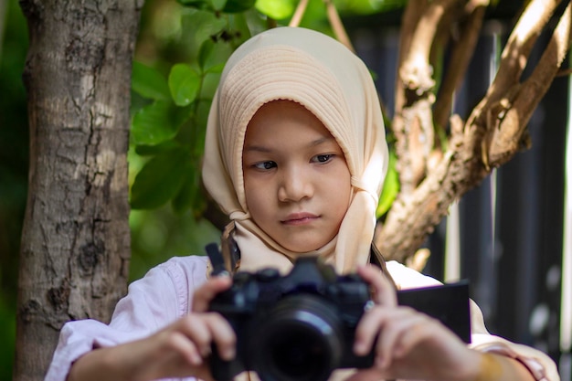 Foto retrato de una niña musulmana asiática sonriente que sostiene una cámara digital al aire libre