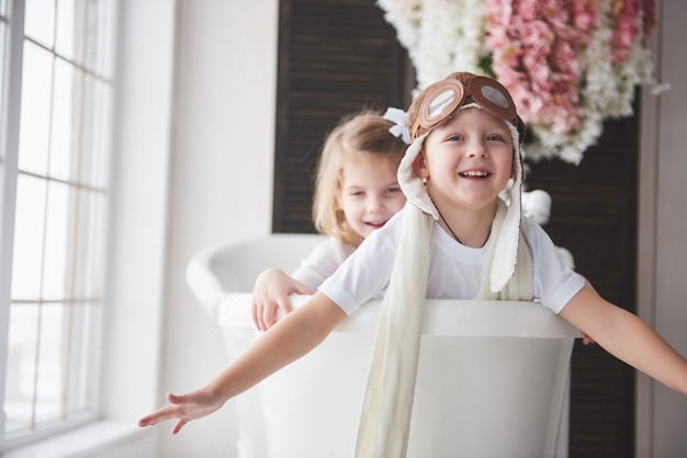 Retrato de una niña y un niño con sombrero de piloto jugando en el baño a los pilotos o marineros. viajes, infancia y realización de sueños.