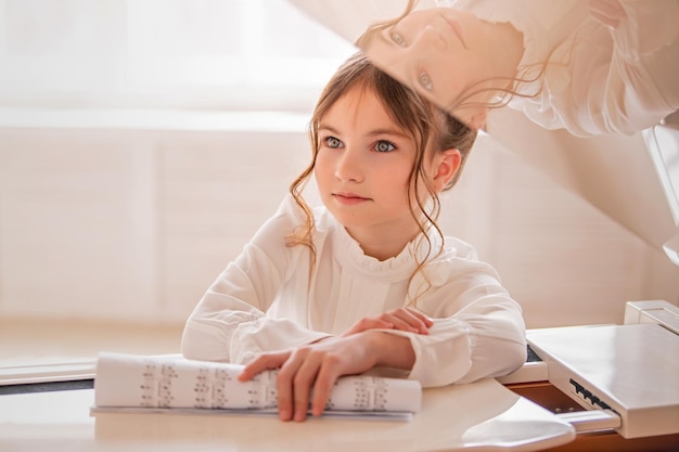 Retrato de una niña con notas en las manos en un gran piano blanco