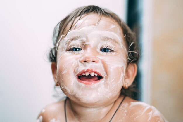 Retrato de una niña de ojos azules toda en crema agria manchada sucia, muy divertida y divertida, los padres pasaron por alto