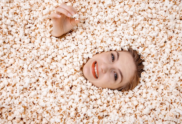 Retrato de niña en palomitas de maíz. Mujer joven enterrada en palomitas de maíz.