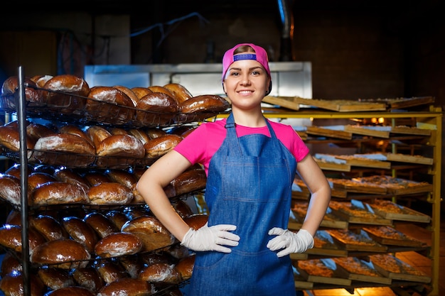 Retrato de una niña panadera en el contexto de los estantes con pan fresco en una panadería. Producción de pan industrial