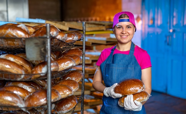 Retrato de una niña panadera con pan en las manos en el contexto de una línea en una panadería. Producción de pan industrial