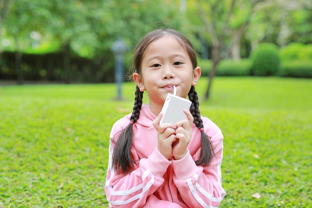 Retrato de niña en paño deportivo beber leche de caja con paja en el parque natural.