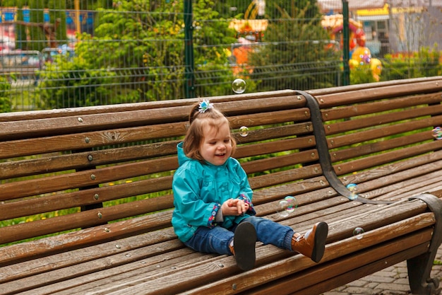 Retrato de una niña en el parque en un banco atrapa pompas de jabón