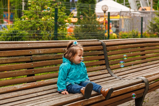 Retrato de una niña en el parque en un banco atrapa pompas de jabón