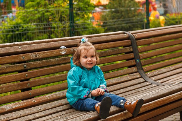 Retrato de una niña en el parque en un banco atrapa pompas de jabón