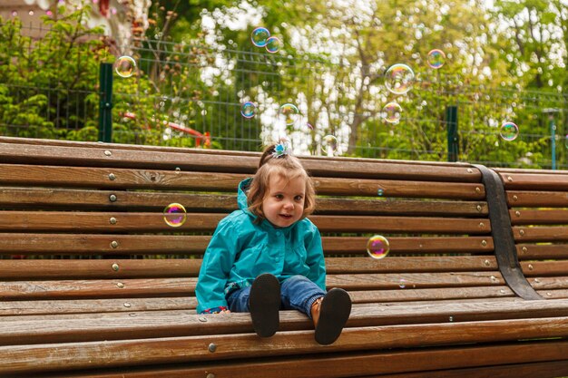Retrato de una niña en el parque en un banco atrapa pompas de jabón