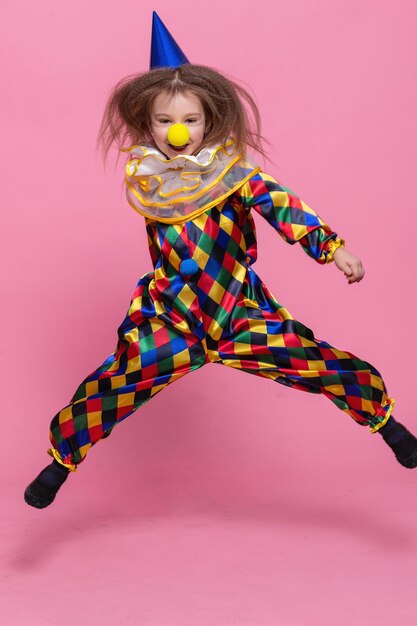 Retrato de niña payaso en traje de payaso saltando sobre un fondo de color rosa