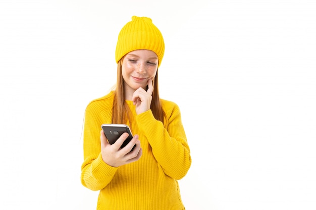 Retrato de una niña pelirroja europea feliz leyendo un mensaje en el teléfono en sus manos