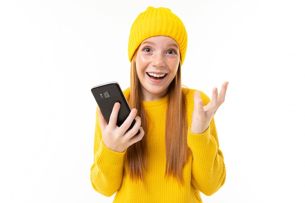 Retrato de una niña pelirroja europea feliz con un teléfono en sus manos sobre un blanco