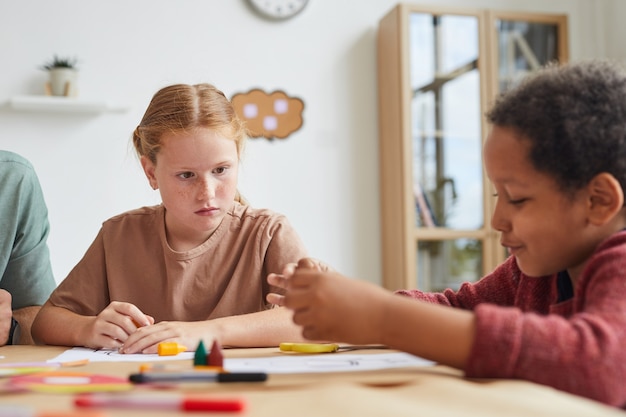 Retrato de niña pelirroja pecosa mirando a un amigo mientras dibujan juntos durante la clase de arte en la escuela