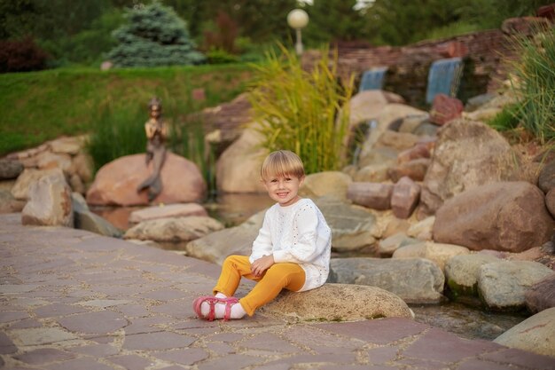 El retrato de una niña con el pelo corto sentada sobre una piedra en el parque