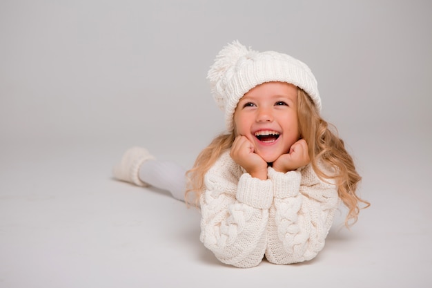 Retrato de una niña de pelo rizado en un gorro de invierno blanco de punto