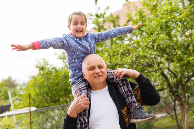 Retrato de una niña pequeña con un abuelo mayor en el jardín trasero, de pie.