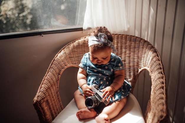 Retrato de una niña pequeña auténtica de raza mixta sentada en una silla de mimbre de ratán con interior en casa