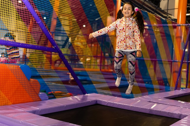 Foto retrato de una niña pequeña y linda jugando y saltando en el trampolín en la sala de juegos para niños, en el patio interior. chica activa divirtiéndose en el centro deportivo.