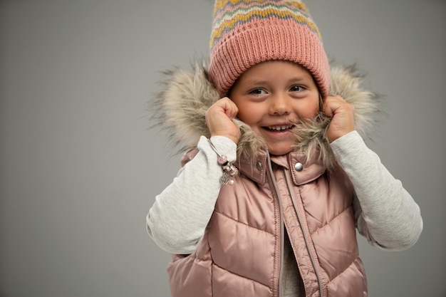 Retrato de una niña pequeña posando con una chaqueta abrigada y un sombrero aislado sobre fondo blanco. Copiar espacio para el anuncio.