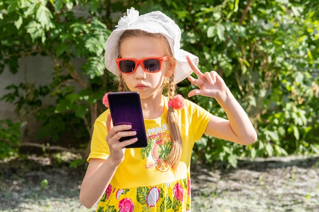 Retrato de niña pequeña tomando un selfie por teléfono inteligente en el parque de verano Una niña alegre con un vestido amarillo