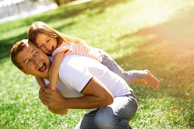 Retrato de niña piggyback montando a su padre en el parque