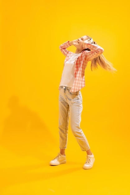 Retrato de niña posando alegremente escuchando música en auriculares aislados sobre amarillo